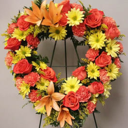 Heart-shaped floral wreath with roses, daisies, carnations, and lilies on a stand
