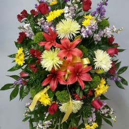 Standing floral spray with red lilies, yellow daisies, and purple accents