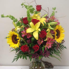 Mixed bouquet with red roses, yellow lilies, and sunflowers in a glass vase