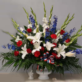 Large red, white, and blue floral arrangement in a white pedestal vase