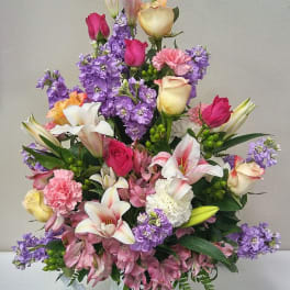 Mixed bouquet of roses, lilies, carnations, and purple flowers in a white vase