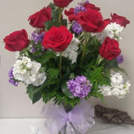 Red roses with white and purple flowers in a glass vase with a lavender bow