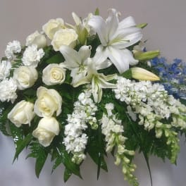 White lilies and roses arranged with blue flowers on a table.