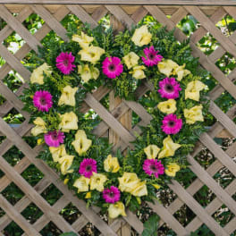 Heart-shaped floral wreath with yellow and pink flowers on a wooden trellis