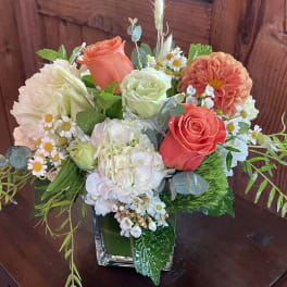Mixed bouquet of coral and white flowers in a square glass vase
