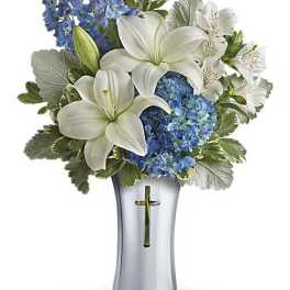 White lilies and blue flowers arranged in a silver vase with a cross