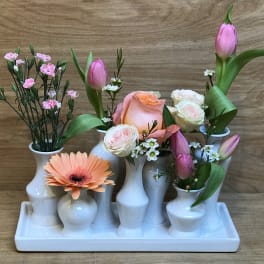 Floral arrangement in white bud vases with pink tulips, roses, and a peach gerbera daisy