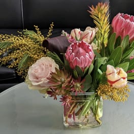 Mixed bouquet with pink protea, tulips, and roses in a clear glass vase