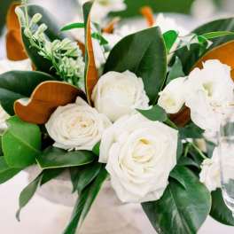 White roses arranged with glossy green leaves and brown accents