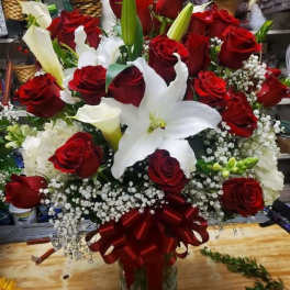 Large bouquet of red roses and white lilies in a glass vase with a red ribbon