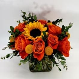 Orange roses and a sunflower arranged in a glass vase