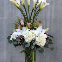 Tall bouquet of white calla lilies, pink roses, and white hydrangeas in a glass vase