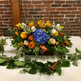 Large floral centerpiece with blue hydrangea, orange blooms, and yellow calla lilies