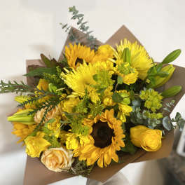 Yellow mixed bouquet with sunflowers, roses, and lilies wrapped in brown paper