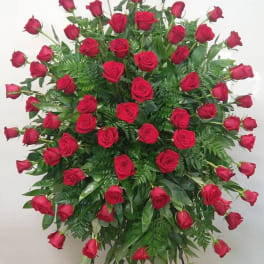 Standing spray of red roses with greenery on a black easel