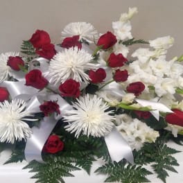 Red roses and white flowers arranged with white ribbon on a table