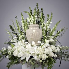 White floral arrangement with lilies and roses around a stone urn