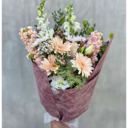 Handheld bouquet of pastel flowers wrapped in mauve paper
