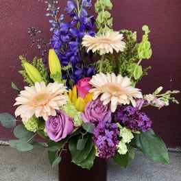 Mixed bouquet with gerbera daisies, roses, and purple blooms in a vase