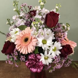 Mixed bouquet of roses, gerbera daisies, and daisies in a red vase