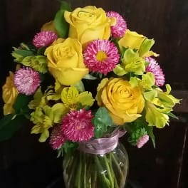 Yellow roses and pink daisies in a glass vase with ribbon