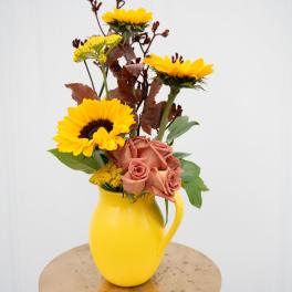 Yellow sunflowers and peach roses in a yellow pitcher vase
