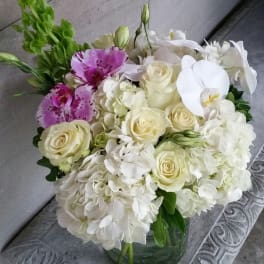 White and cream bouquet with pink orchids in a glass vase