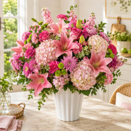 Pink lilies and mixed blooms arranged in a white vase