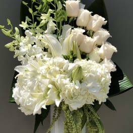 White floral arrangement with roses, lilies, and orchids on a pedestal