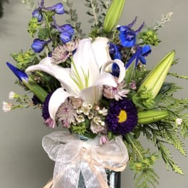 Blue and white floral arrangement in a glass vase with a sheer bow