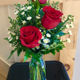 Three red roses with small white daisies in a glass vase