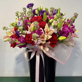 Mixed bouquet of red roses, lilies, and purple flowers in a black vase