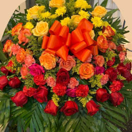 Large floral spray of red, orange, and yellow roses with a bright ribbon bow
