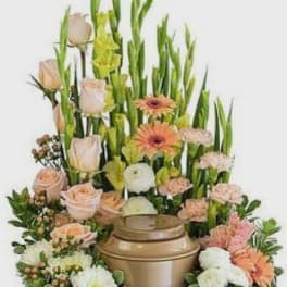 Tall floral arrangement with peach roses, gerbera daisies, and white blooms in a bronze urn