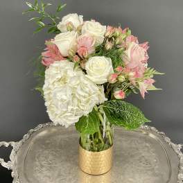 White and blush bouquet in a clear glass vase with a gold base