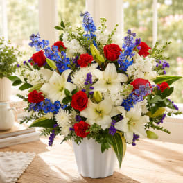 Mixed bouquet of red roses, white lilies, and blue flowers in a white vase