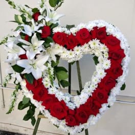 Heart-shaped floral tribute with red roses and white lilies on an easel