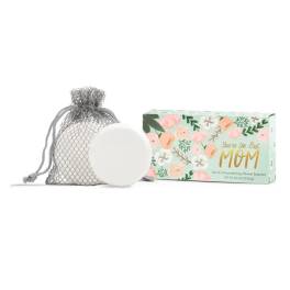 A mesh bag with a white shower steamer beside a floral gift box.