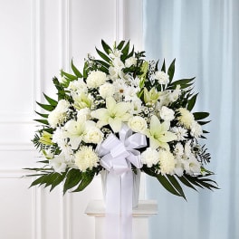 White floral arrangement with lilies, roses, and chrysanthemums in a vase with a white ribbon