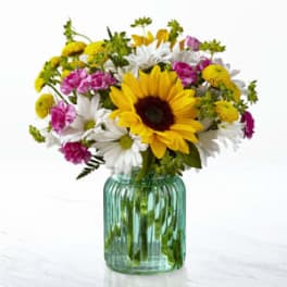 Bouquet of sunflowers, white daisies, and pink flowers in a green glass vase