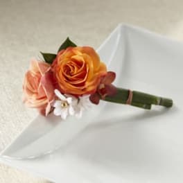 Small boutonniere with orange and peach roses on white fabric