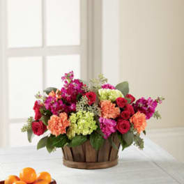 Mixed bouquet of red, pink, peach, and green flowers in a wooden basket