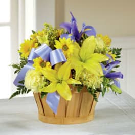 Yellow lilies and purple flowers in a wooden basket with a blue ribbon