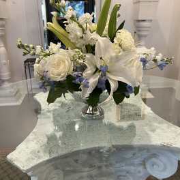 Low white and blue flower arrangement with lilies and roses in a silver pedestal vase
