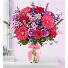 Bouquet of pink gerbera daisies and red roses in a glass vase with a pink ribbon