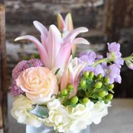 Pink lilies and roses arranged in a glass vase with white blooms