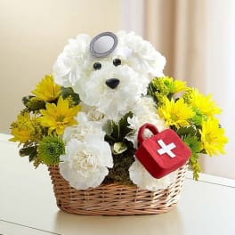 White teddy bear floral arrangement in a wicker basket with yellow flowers and a red first-aid bag