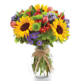 Bouquet of sunflowers, tulips, and purple daisies in a glass vase