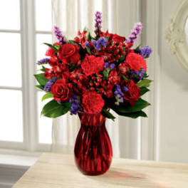 Red roses and carnations in a red vase with purple accents