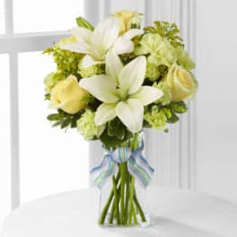 White lilies and pale yellow roses in a clear glass vase with a striped ribbon